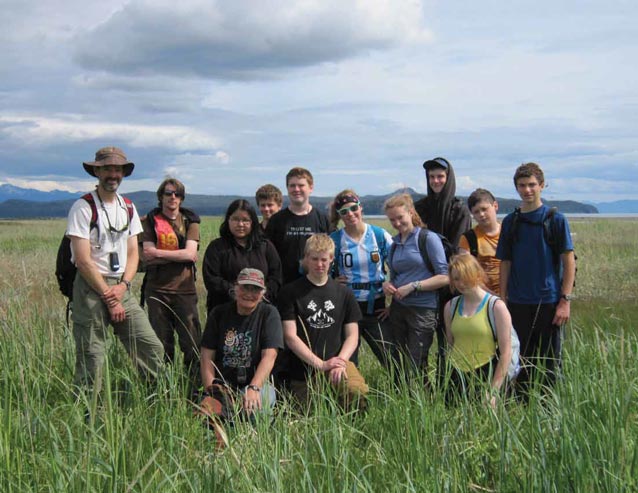 several adults and teens standing together in a grassy field