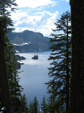 A view framed by vegetation to sparkling Crater Lake, surrounded by steep topography. A view framed by vegetation to sparkling Crater Lake, surrounded by steep topography.