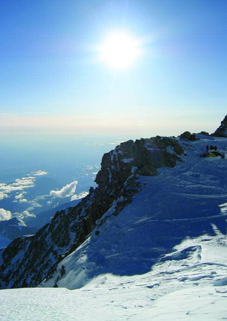 snowy mountain under a sunny sky looking down at thick smoke plumes