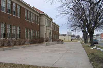 A two-story red brick school opens onto a concrete courtyard. A two-story red brick school opens onto a concrete courtyard.
