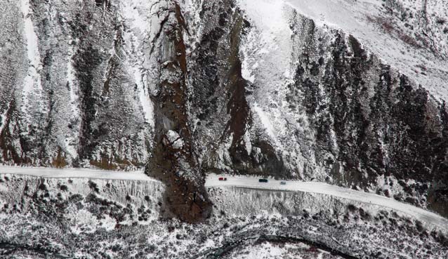 snow-dusted hillside with a large landslide across a snowy road, three cars parked nearby snow-dusted hillside with a large landslide across a snowy road, three cars parked nearby