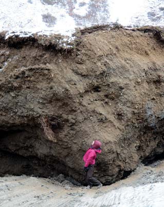 woman standing near a block of frozen soil three times her height