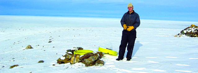 man standing on a tree-less snowy hilltop near a pile of rocks