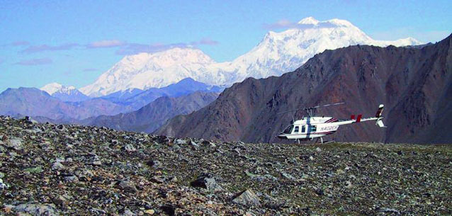 helicopter parked on a rocky ridge, steep mountains in the distance