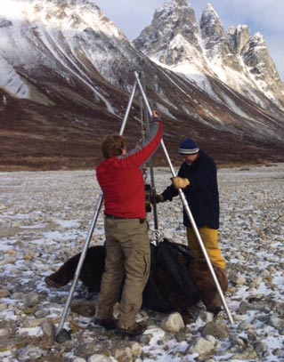 two people weighing a bear on a tripod scale, mountains in the background two people weighing a bear on a tripod scale, mountains in the background