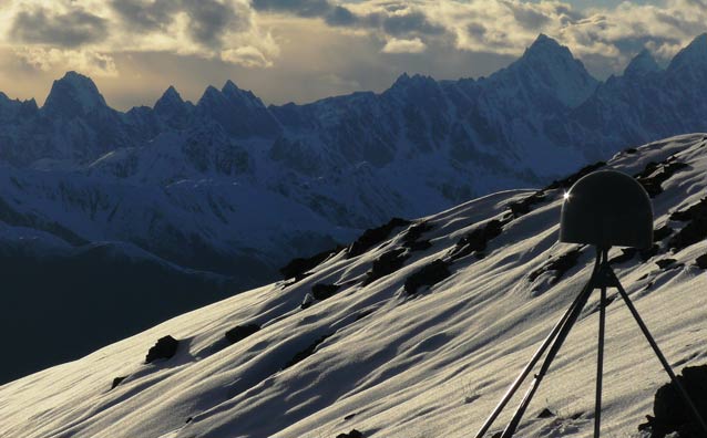 a domed device on a tripod, mounted on a snowy, rocky mountainside