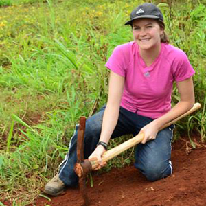 Researcher with a pick kneels on a dirt slope