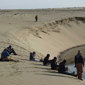 Students sit on the edge of a sand dune