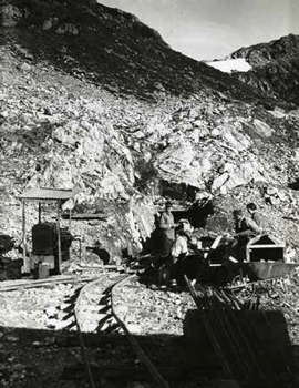 men standing near a rustic railroad track leading into a tiny tunnel in a mountainside men standing near a rustic railroad track leading into a tiny tunnel in a mountainside