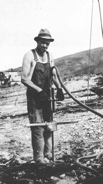 man in overalls standing next to a device stuck in the ground man in overalls standing next to a device stuck in the ground