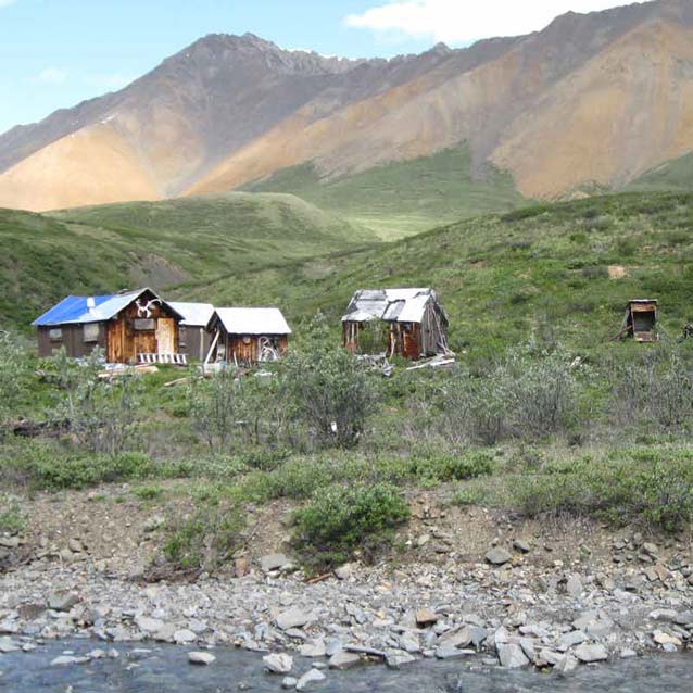 three rustic buildings near a creek with hills and mountains in the distance three rustic buildings near a creek with hills and mountains in the distance
