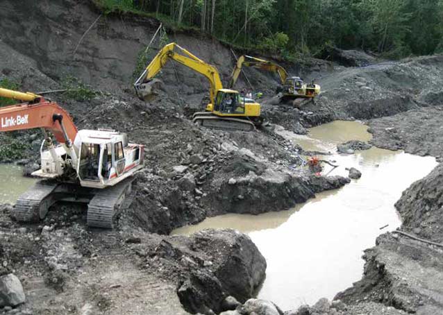 three backhoes digging near a muddy creek