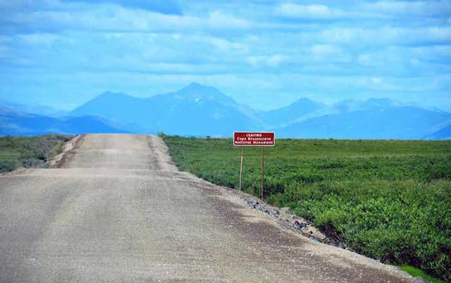 dirt road leading across a tree-less plain toward distant mountains