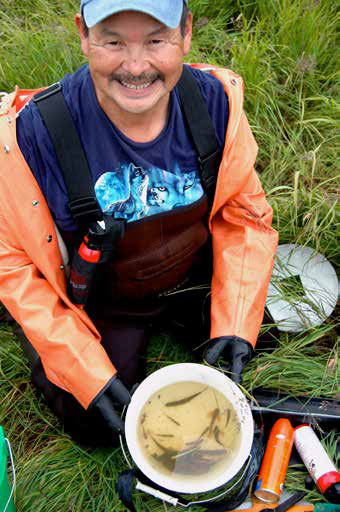smiling man kneeling in front of a bucket with fish in it