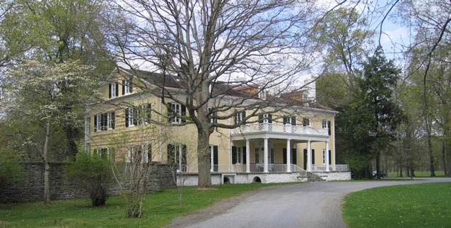 A driveway curves in front of a large Federal style mansion, symmetrical with flat facades.