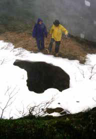 two people standing over a mine opening in the ground two people standing over a mine opening in the ground