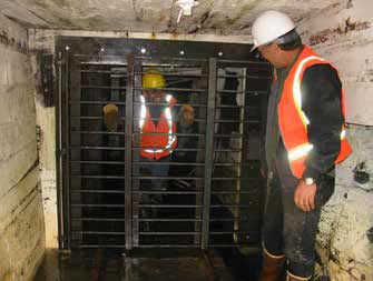 two men standing on either side of a metal gate inside a tunnel two men standing on either side of a metal gate inside a tunnel