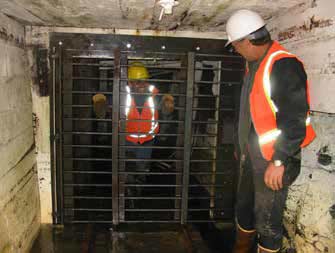 two men standing on either side of a metal gate inside a tunnel