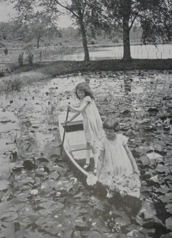 Two young girls in white dresses paddle through a pond dense with water lilies. Two young girls in white dresses paddle through a pond dense with water lilies.
