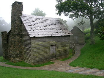 The Brinegar Cabin has two stone chimneys, wooden siding, and a shingled roof.