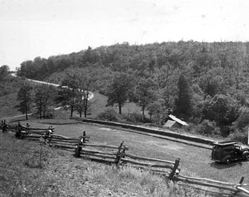 A split-rail fence surrounds a parking lot with a single car.