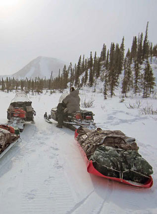 man in winter attire sitting on a snowmobile in a snowy forest