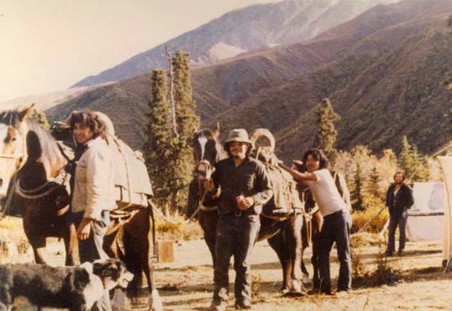 four men and a dog near two horses