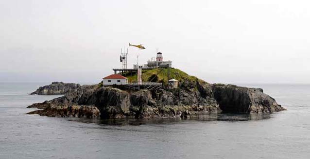 small rocky island with a lighthouse and helicopter about to land on it