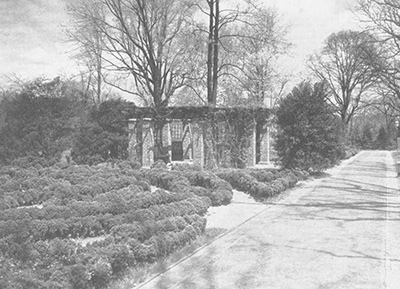 Low rows of boxwood weave back and forth in front of a brick pergola.