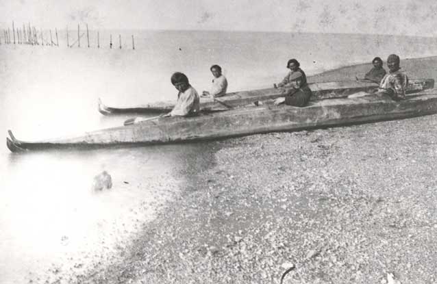six people sitting in two long kayaks on a gravelly beach six people sitting in two long kayaks on a gravelly beach