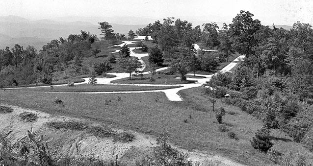 A paved loop winds through grass and trees of a level ridge top, with hills visible in the distance.