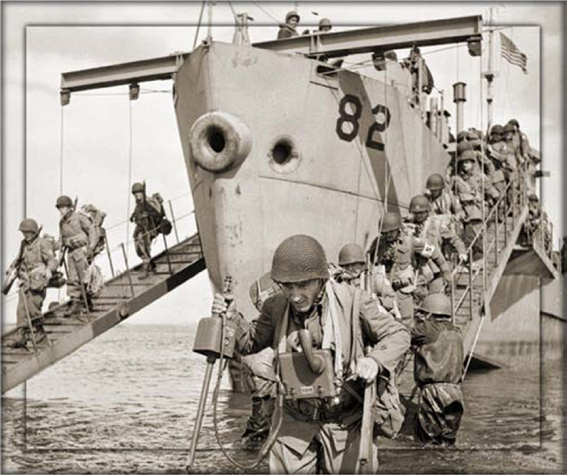 Soldiers walk down ramp next to ship fully loaded in gear.