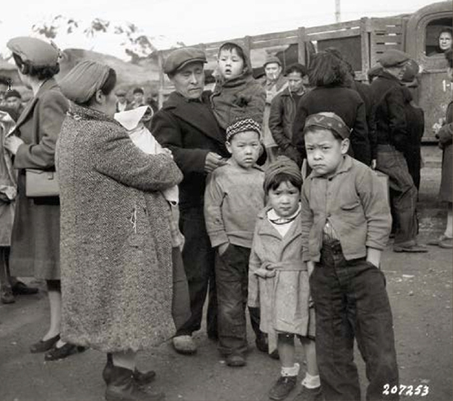 An Aleut family stands by truck. Four children look towards camera.