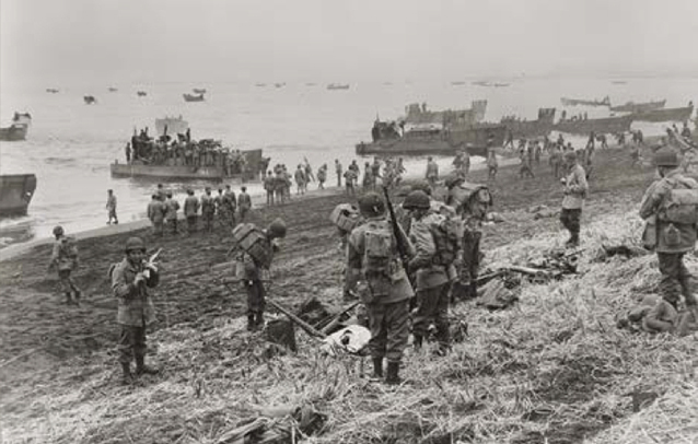 Soldiers on beach carrying items from boats.