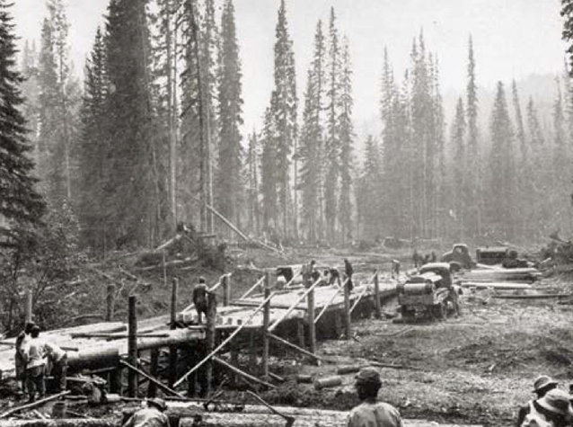 Road construction crews stand on wooden platform.