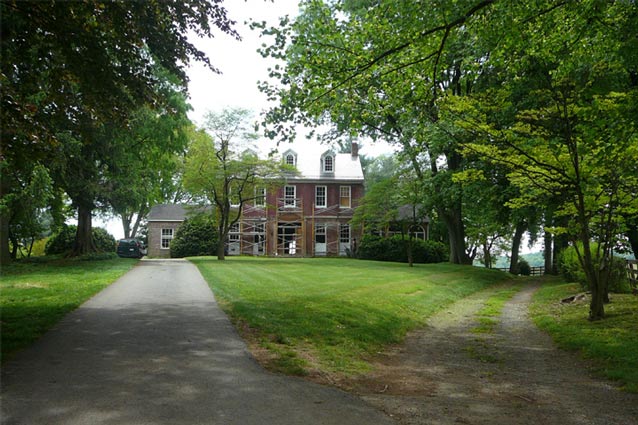 Gravel tracks curve to the right from a paved driveway, which leads towards a tall brick farmhouse. Gravel tracks curve to the right from a paved driveway, which leads towards a tall brick farmhouse.