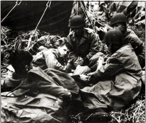 Four soldiers gather around a fifth soldier and rub his feet.