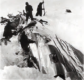 snow covered wreckage of silver plane with men around it