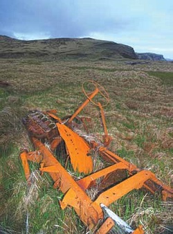 Rusting metal frame with steering wheel in grass.