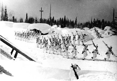 B&W photo of soldiers in white with skis over their shoulder