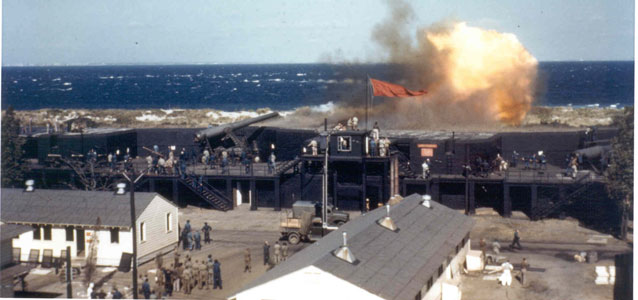 color photo of large explosion atop fort walls, ocean beyond