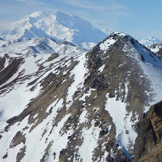 a vast white mountain looming behind nearer rocky peaks partly covered in snow