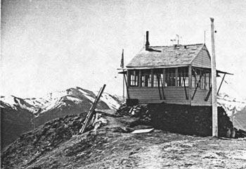 B&W; small white building with radio antennae and mtns in back