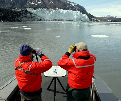 Two people on a boat looking through binoculars.