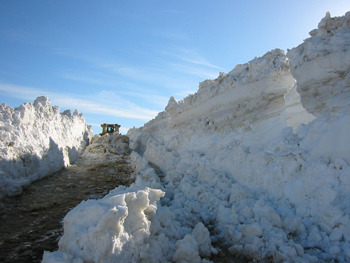 a bulldozer plows through snow that towers over it