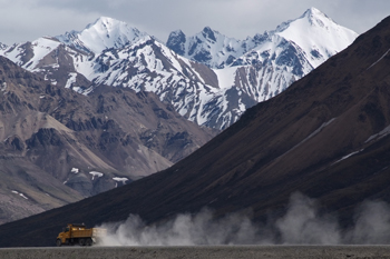 A dump truck kicks up a cloud of dust on a dirt road