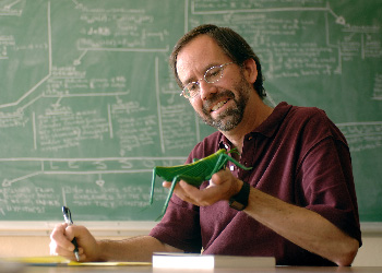In front of a green chalkboard, a man makes handwritten notes from a scale model of a grasshopper In front of a green chalkboard, a man makes handwritten notes from a scale model of a grasshopper
