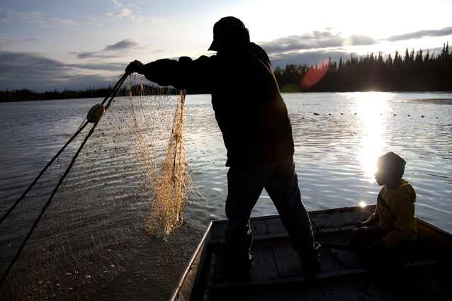 a man pulls in a fishing net while a small boy watches