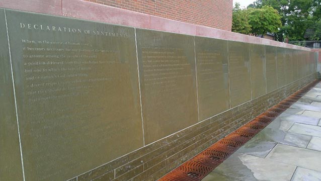 Words are etched onto a long, flat bluestone wall with water cascading down its surface.