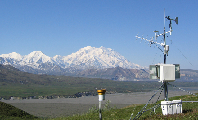 a weather station stands on a hillside with Denali in the background